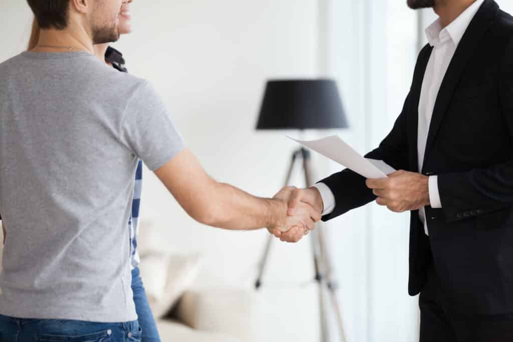 man in gray shirt shakes hands with landlord in suit holding paper