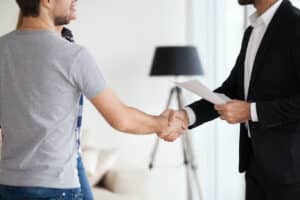 man in gray shirt shakes hands with landlord in suit holding paper