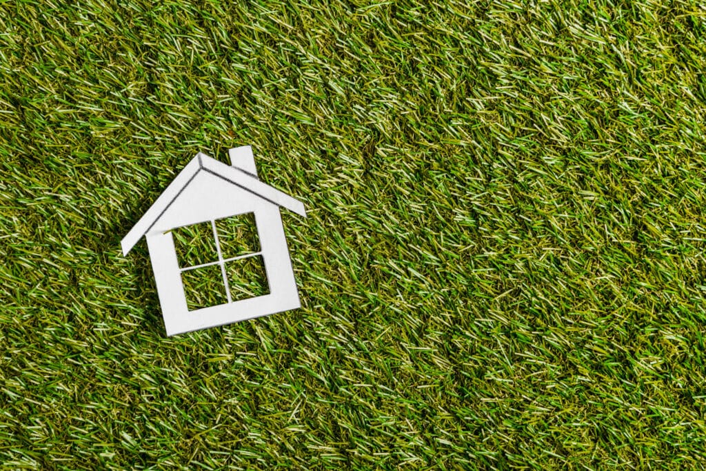 top view of white paper house on green grass, energy efficient home concept